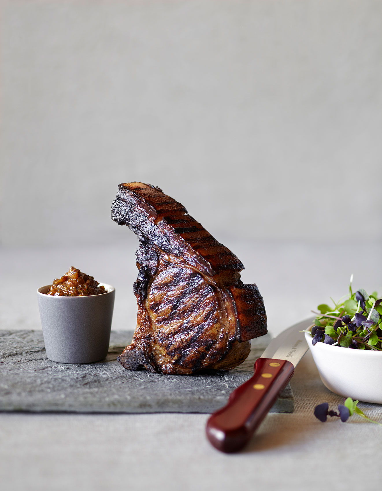 Vanilla Table • Standing Grilled Pork Chop on Stone Block with Steak Knife • Cookbook & Editorial Food Photography