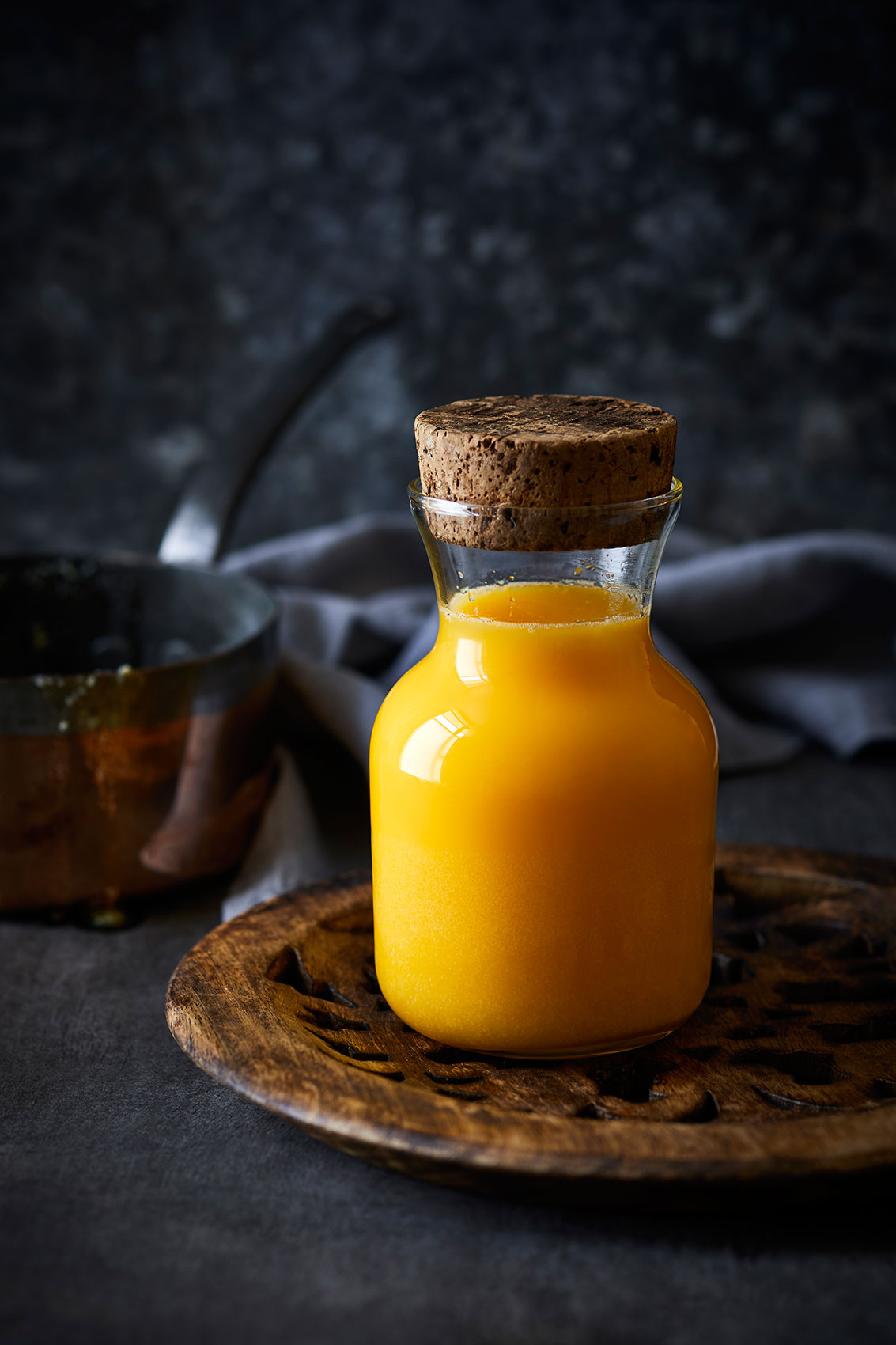 My Indian Kitchen •  Corked Glass Bottle of Ghee on Wooden Dish • Cookbook & Editorial Food Photography