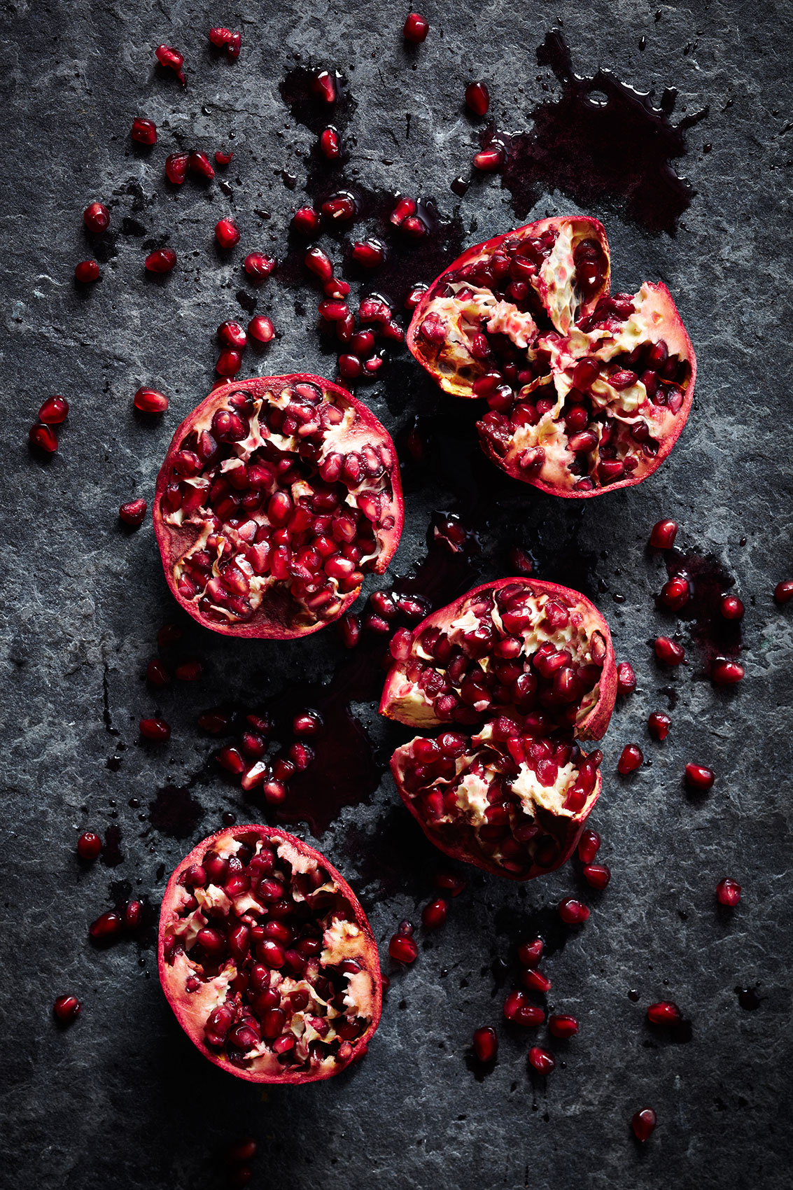 Spice Health Heroes • Crushed Red Pomegranate Halves on Dark Stone Bench • Cookbook & Editorial Food Photography